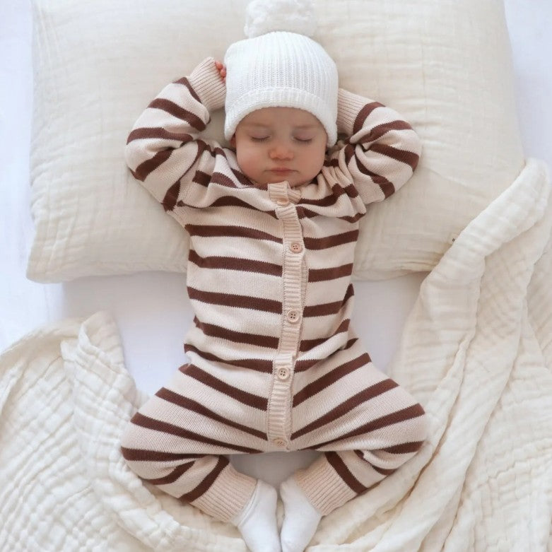 Baby in a striped outfit and white hat lying on a soft surface