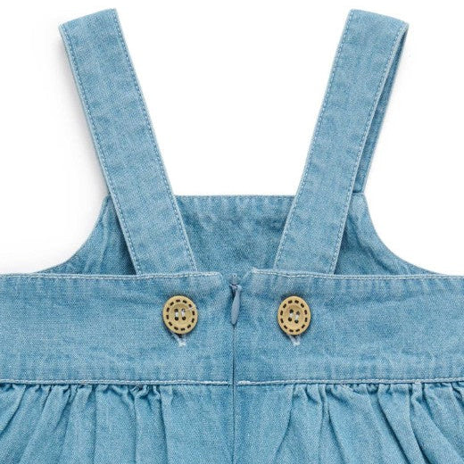 Close-up of a blue denim dress with straps and buttons on a white background