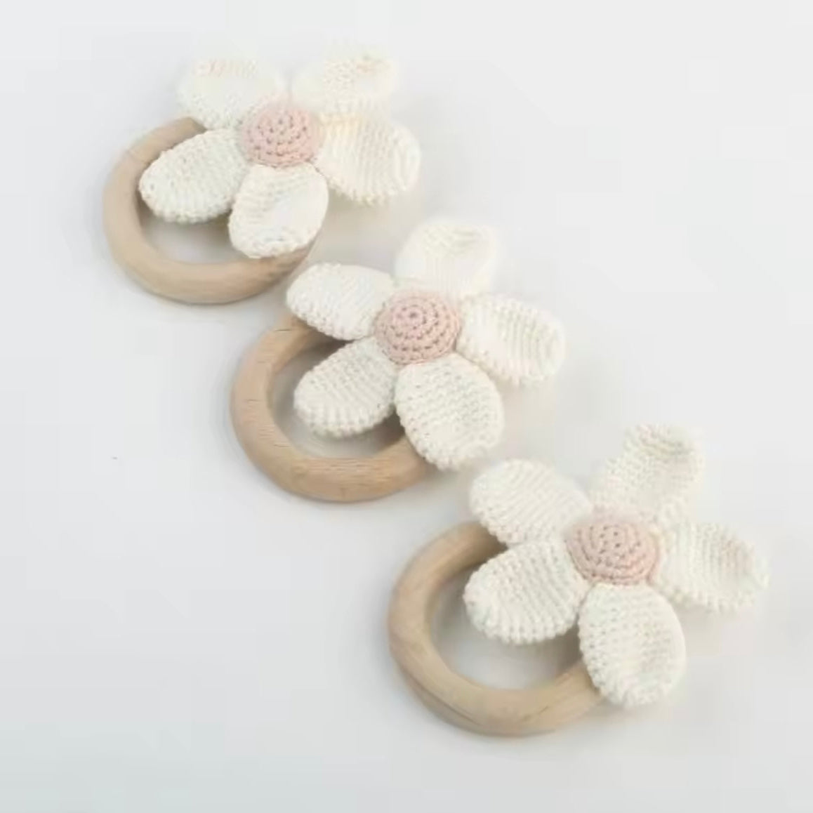 Three wooden rings with crocheted flower attachments on a light gray background