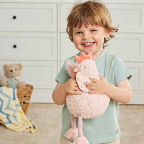 Child holding a pink plush toy in a room with a basket of toys in the background
