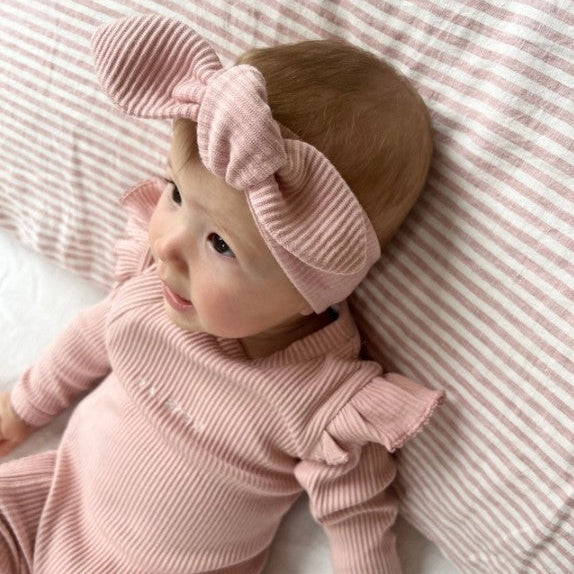 Baby in pink ribbed outfit and headband lying on a striped pink blanket