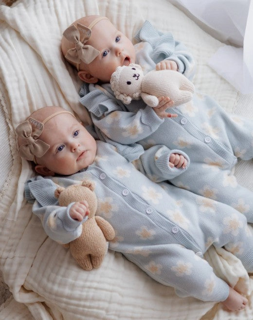 Two babies in matching outfits with teddy bears on a soft surface