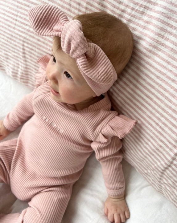 Baby in pink ribbed outfit and headband lying on a striped pink blanket