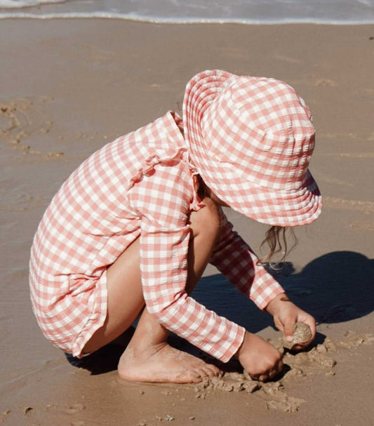 Child in a pink checkered outfit playing in the sand on a beach